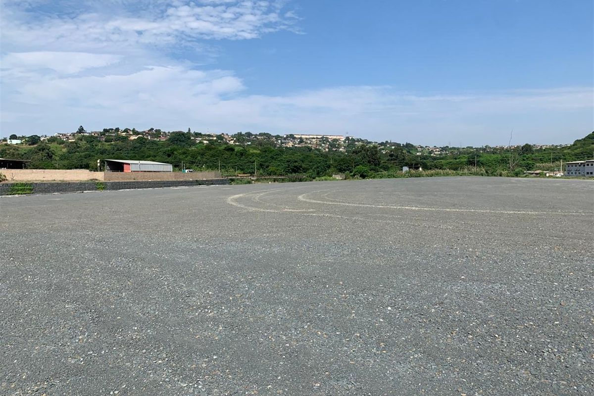 A large, level commercial land plot featuring a gravel surface and a retaining wall, offering expansive views of the surrounding landscape.