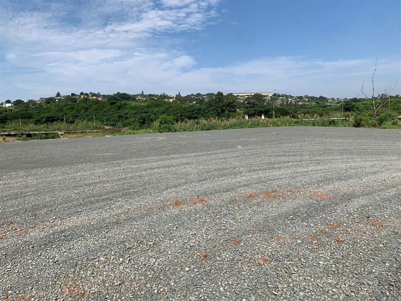 A wide-angle view of a level, gravel-surfaced commercial vacant land plot with surrounding landscape views.