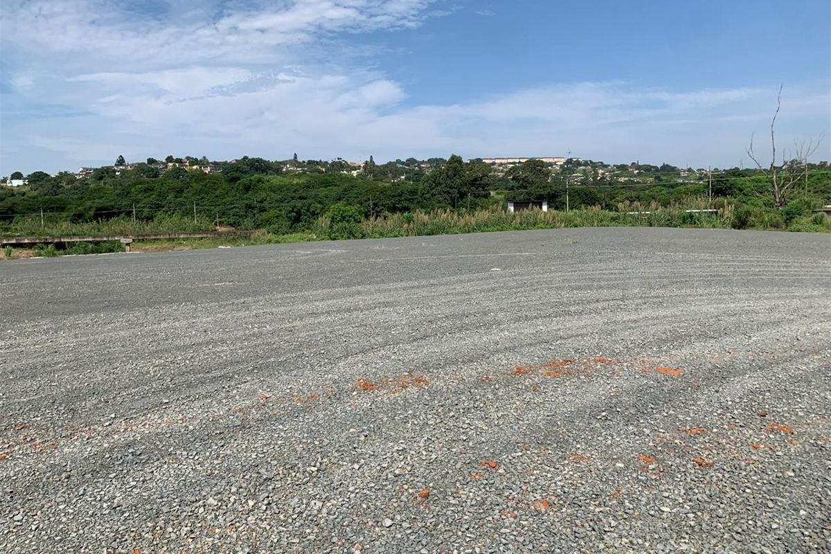 A wide-angle view of a level, gravel-surfaced commercial vacant land plot with surrounding landscape views.