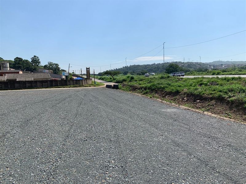 A wide-angle view of a vacant commercial land plot featuring a leveled gravel surface and surrounding infrastructure.