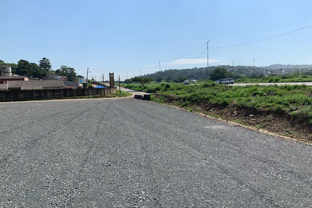 A wide-angle view of a vacant commercial land plot featuring a leveled gravel surface and surrounding infrastructure.