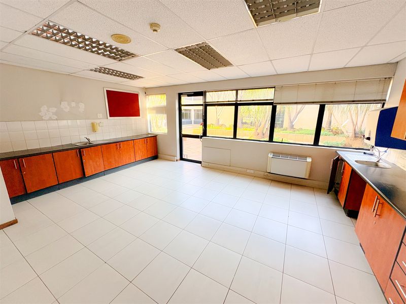 A functional office kitchenette featuring laminate cabinetry, tiled flooring, and a drop ceiling with integrated lighting, offering a clean and practical workspace.