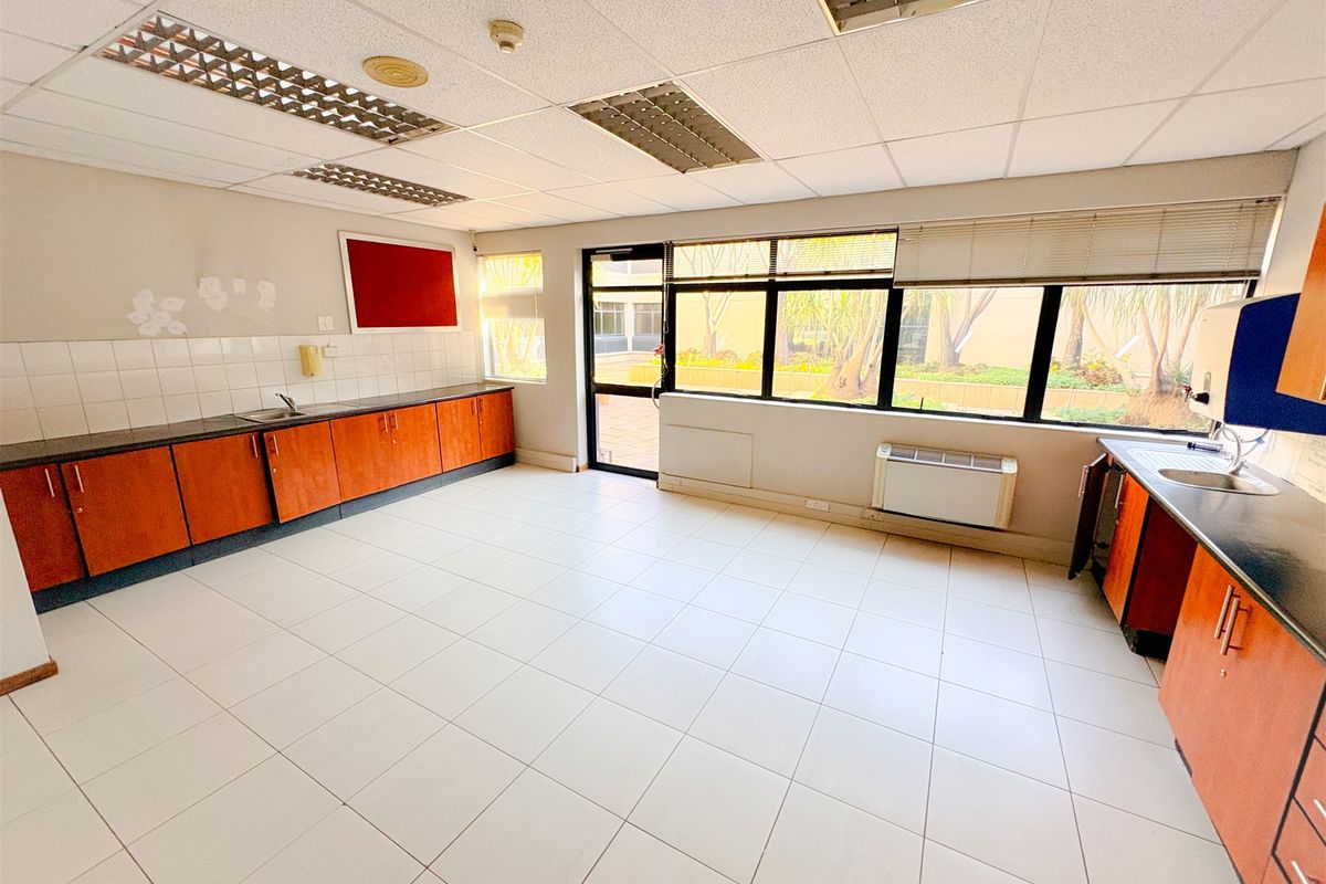 A functional office kitchenette featuring laminate cabinetry, tiled flooring, and a drop ceiling with integrated lighting, offering a clean and practical workspace.