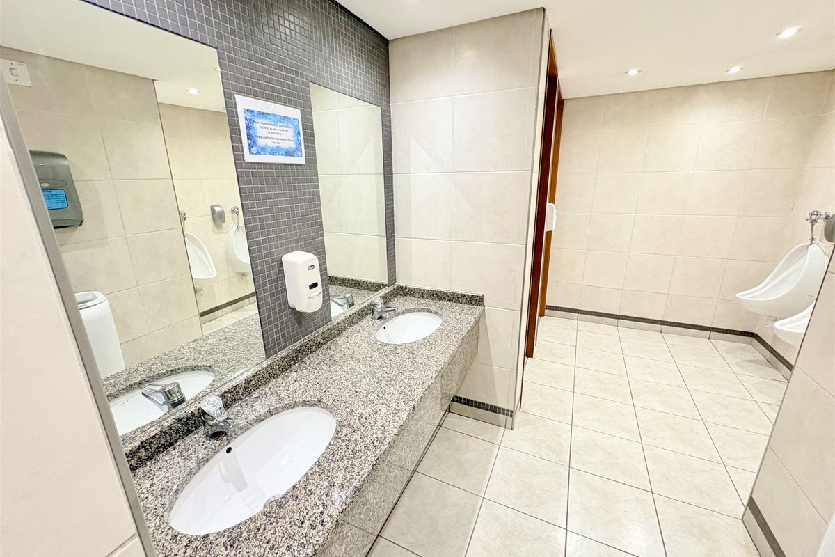 A clean, modern commercial bathroom featuring a dual vanity with granite countertops, undermount sinks, and wall-mounted urinals with neutral ceramic tiling.
