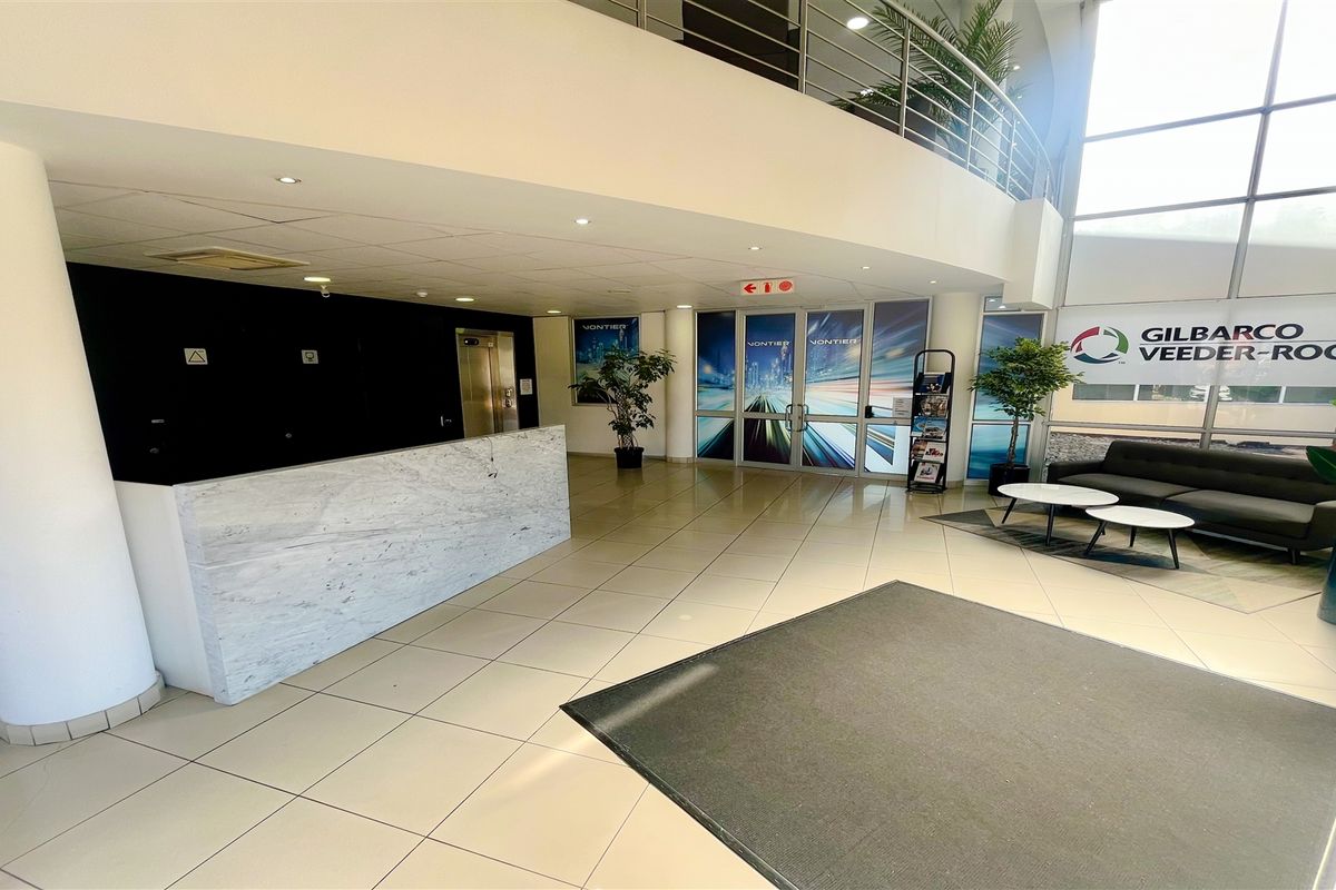 Spacious office building entrance featuring a marble-finish reception desk, double-volume ceiling, large glass windows, and access to an elevator.