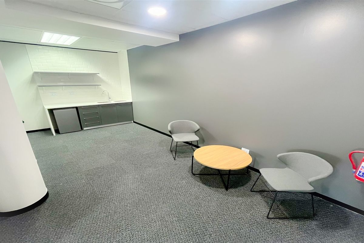 A modern office space featuring a compact kitchenette with built-in cabinetry, sink, and recessed lighting, providing a functional break area.