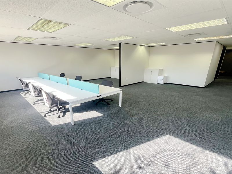 A spacious open-plan office area featuring carpeted flooring, suspended ceilings with recessed lighting, and a functional partition wall.