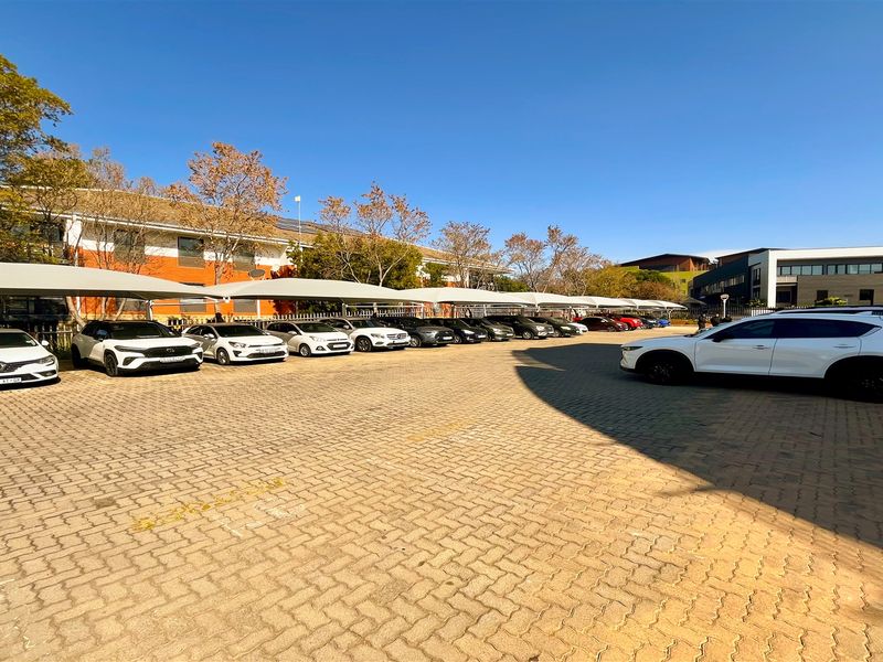 A spacious paved parking area featuring multiple shade cloth carports, providing ample covered parking for office staff and visitors.