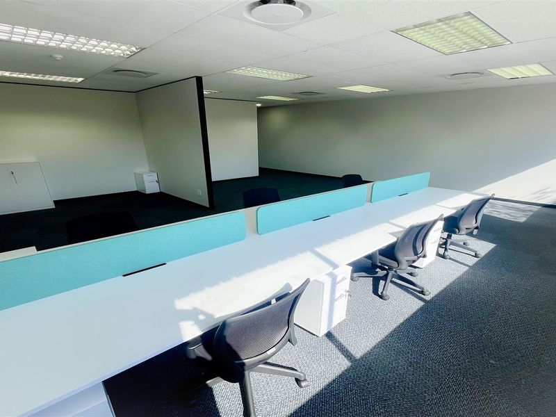 A bright, open-plan office space featuring a neutral color palette, fitted carpeting, and recessed ceiling lighting, providing a professional and functional work environment.