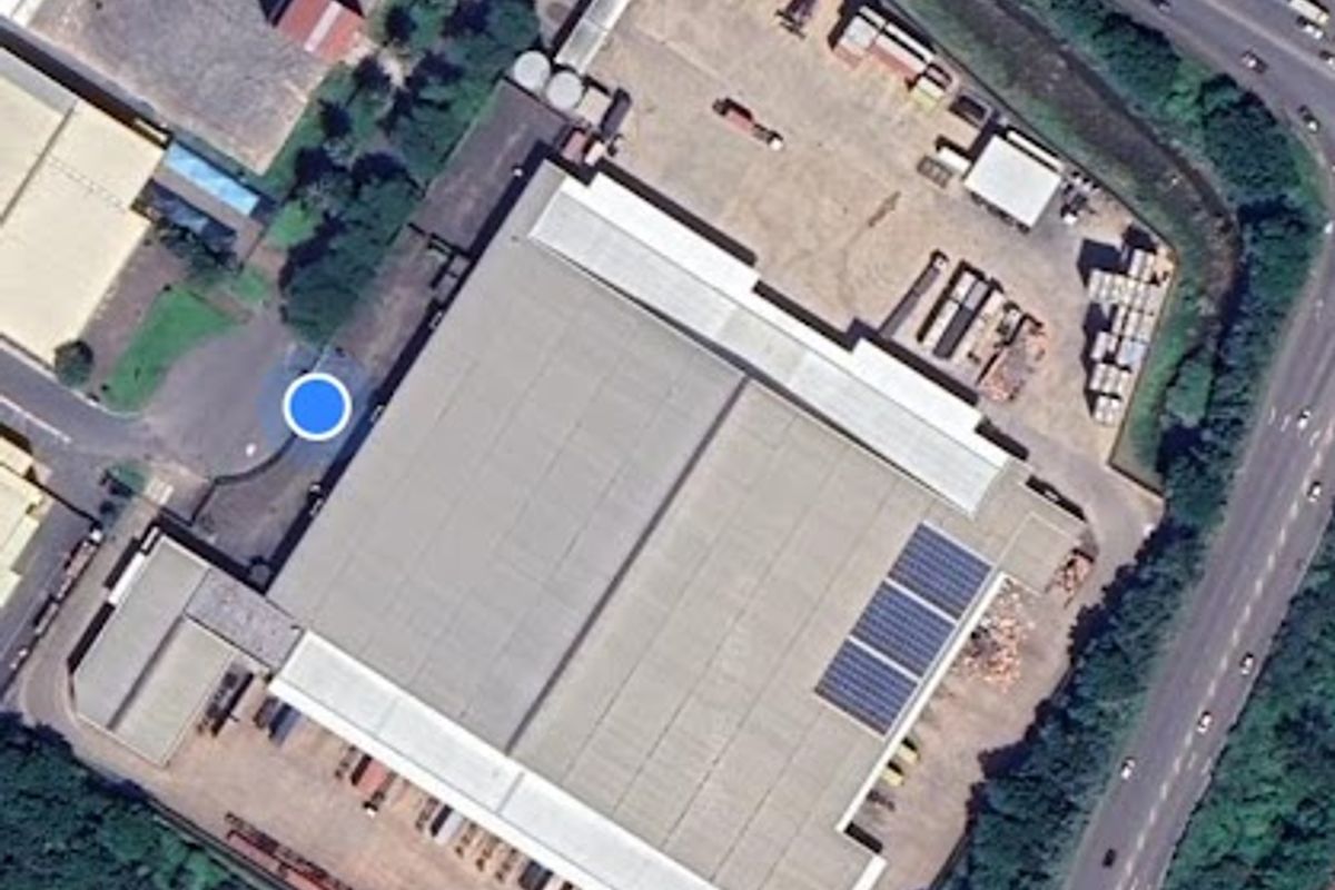 Aerial view of an industrial property featuring a large warehouse building with solar panels, paved yard space, and convenient access to major road networks.