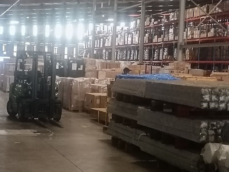Large industrial warehouse space featuring high ceilings with exposed steel trusses, concrete flooring, and extensive pallet racking systems for storage.