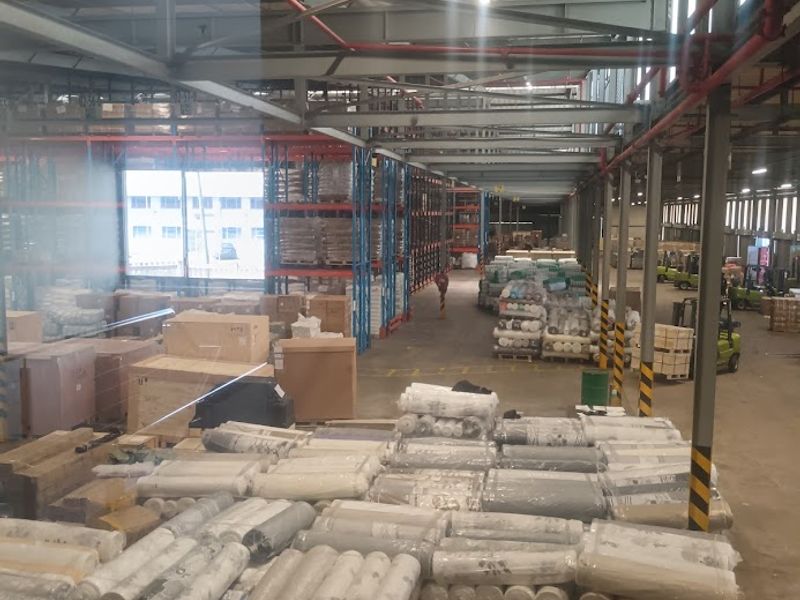 Large industrial warehouse space featuring high ceilings with exposed steel trusses, fire sprinkler systems, and extensive heavy-duty racking for storage.