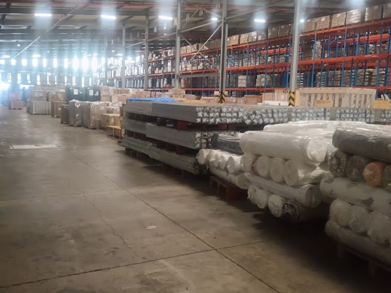 Large industrial warehouse space featuring high ceilings, exposed steel structural elements, concrete flooring, and extensive heavy-duty racking systems for storage.