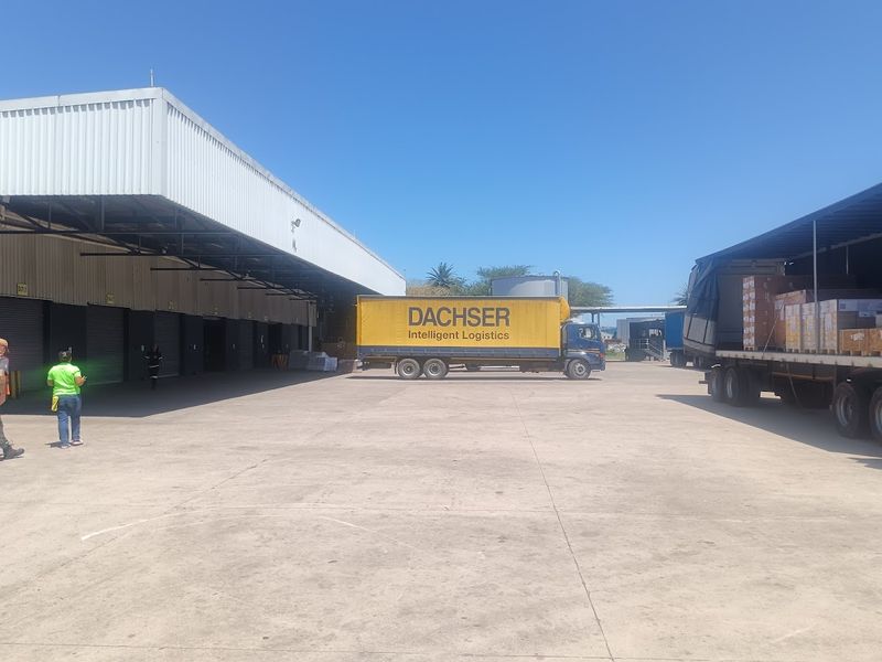 Industrial loading yard featuring a large concrete apron, metal roof canopy, and multiple roller shutter doors for logistics operations.