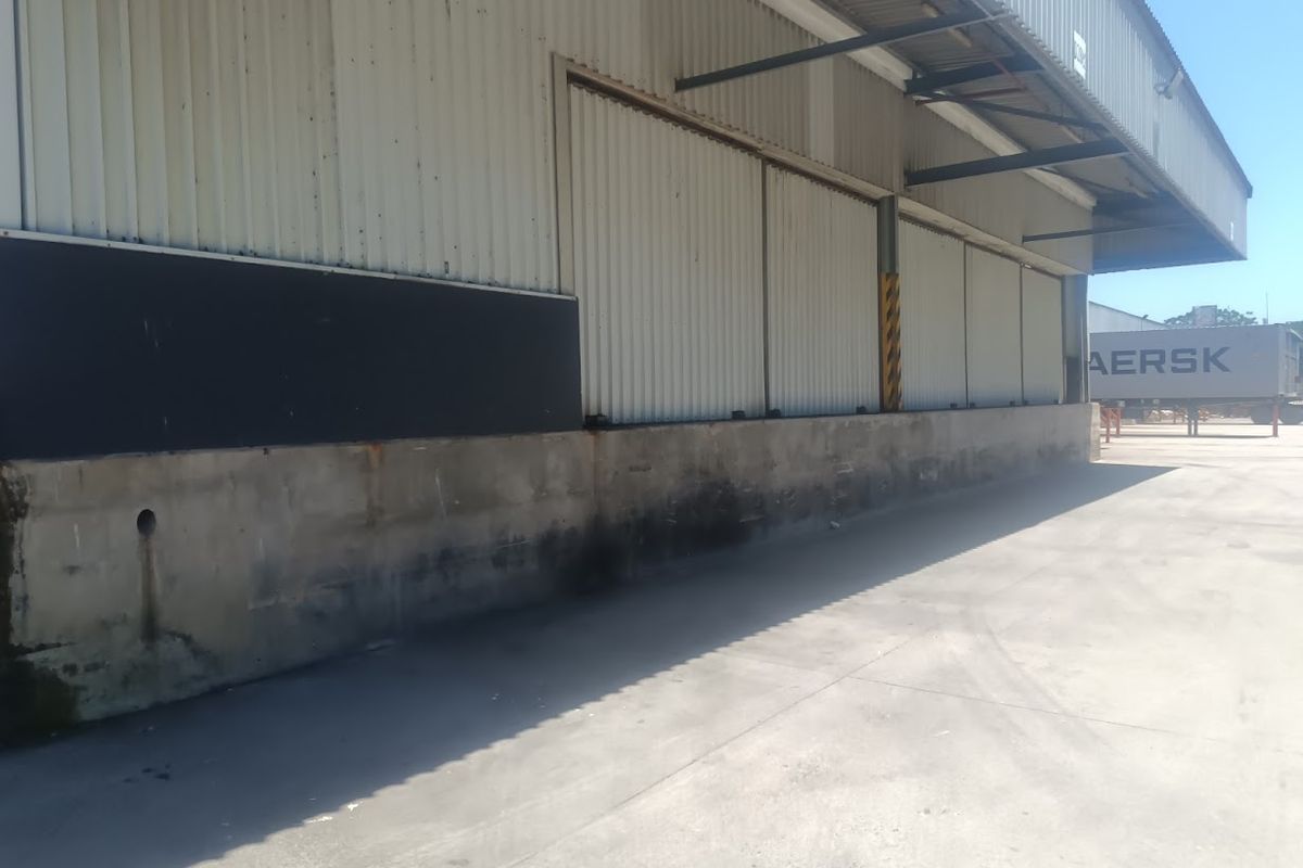 Industrial exterior view showing a concrete loading dock area with corrugated metal cladding and a steel roof overhang.