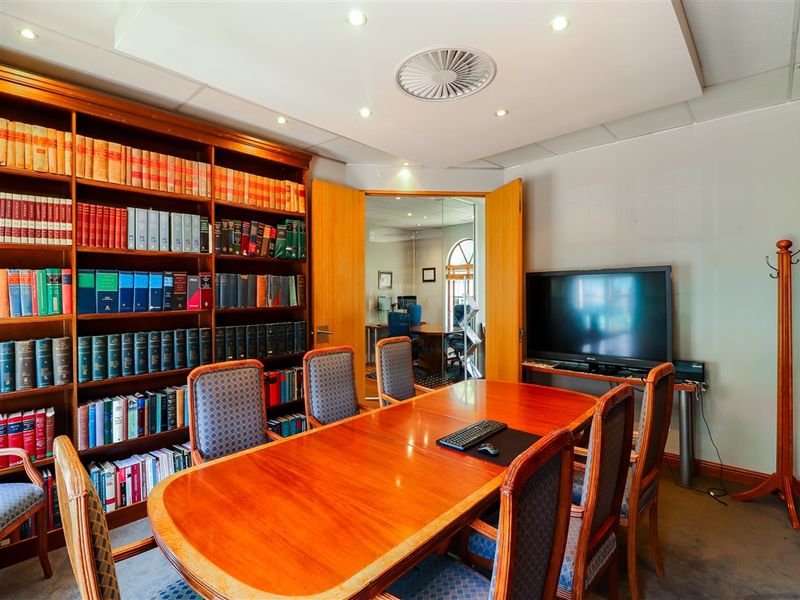 A professional office or boardroom featuring extensive built-in wooden shelving, recessed ceiling lighting, and double door access to an adjacent workspace.