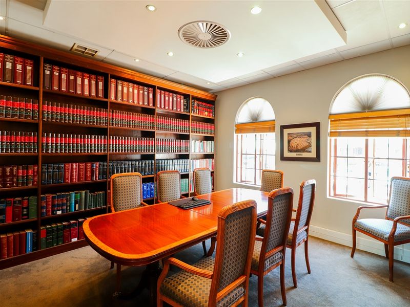 A professional office or boardroom featuring extensive built-in wooden library shelving, arched windows, and recessed ceiling lighting in a well-maintained commercial space.