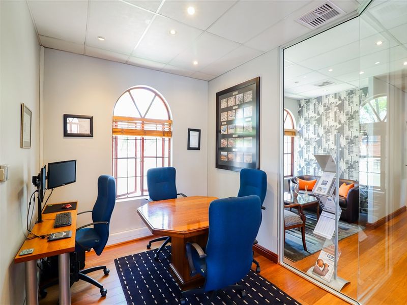A professional office space featuring timber flooring, a suspended ceiling with recessed lighting, and a modern glass partition wall overlooking an adjacent room.