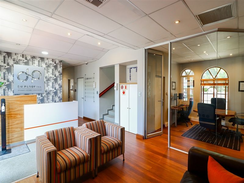 Professional commercial office reception area featuring timber flooring, a built-in reception desk, and a glass-partitioned private office space.