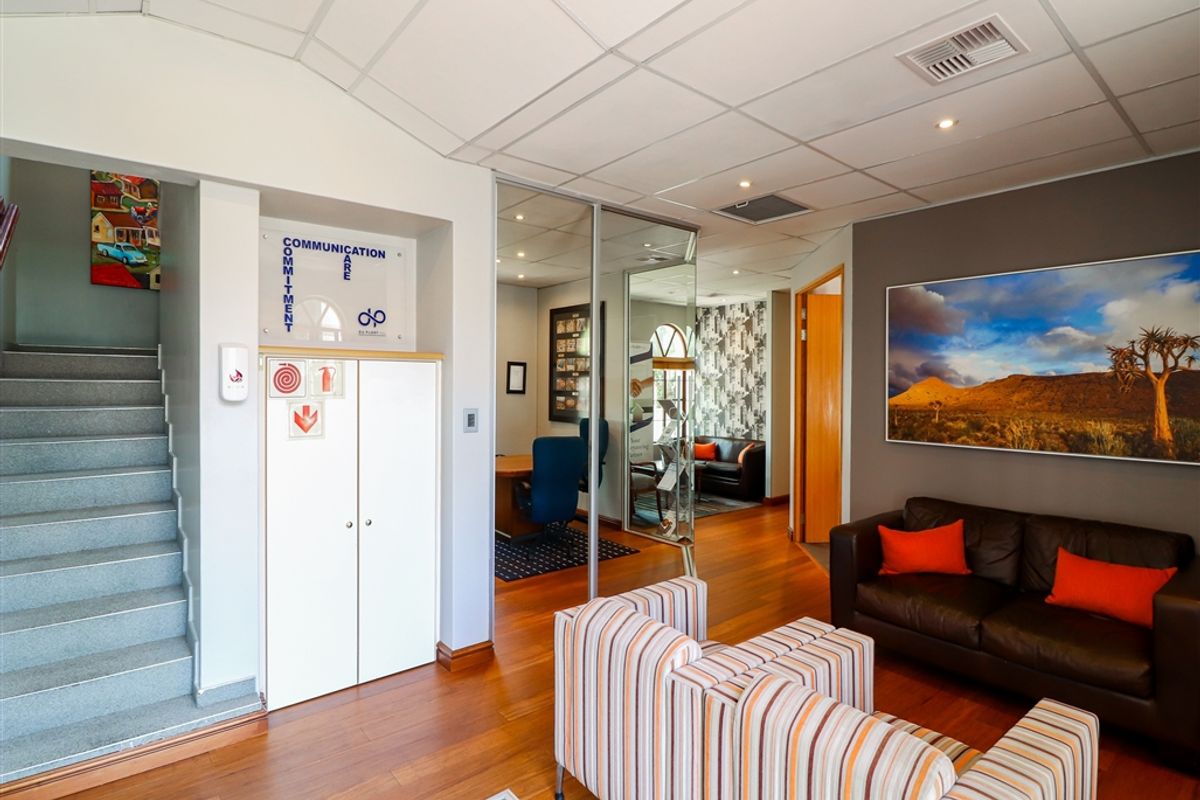 Professional commercial reception area featuring hardwood flooring, a glass-partitioned office space, built-in storage, and a staircase leading to an upper level.