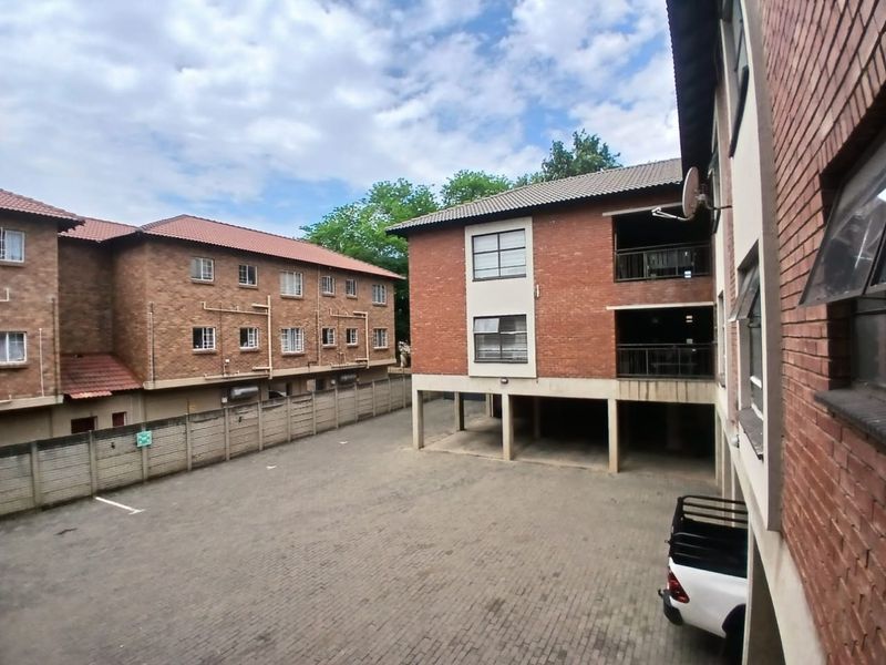 Exterior view of a multi-story commercial or residential complex featuring face-brick facades, covered parking bays, and a paved courtyard area.