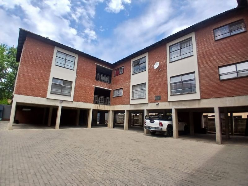 Exterior view of a multi-story commercial brick building featuring covered ground-level parking bays and metal-framed windows.