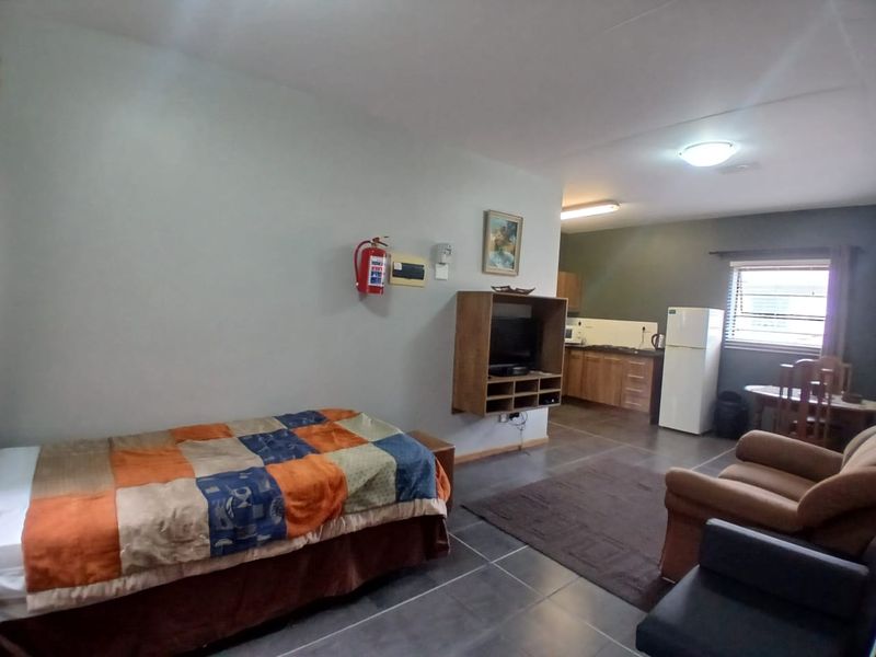 An open-plan studio apartment featuring a combined living and sleeping area with an adjacent kitchenette, tiled flooring, and a wall-mounted fire extinguisher.