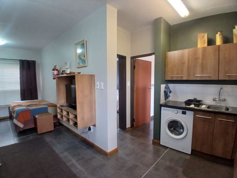 Compact open-plan studio unit featuring a kitchenette with built-in cabinetry, integrated laundry space, and tiled flooring throughout.