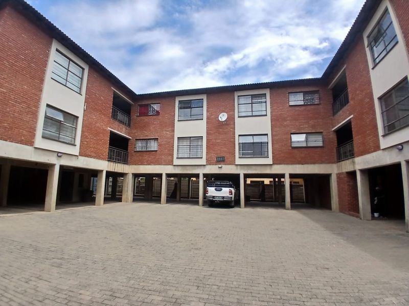 Exterior view of a multi-story commercial or residential complex featuring exposed brick facade, covered ground-level parking area, and paved courtyard.