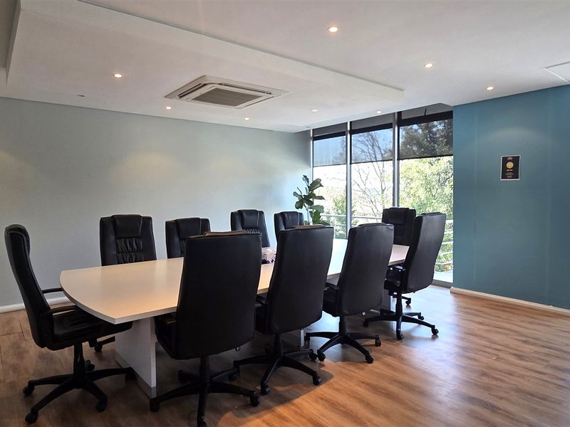 A professional office boardroom featuring laminate wood flooring, recessed ceiling lighting, integrated air conditioning, and large windows providing natural light and exterior views.