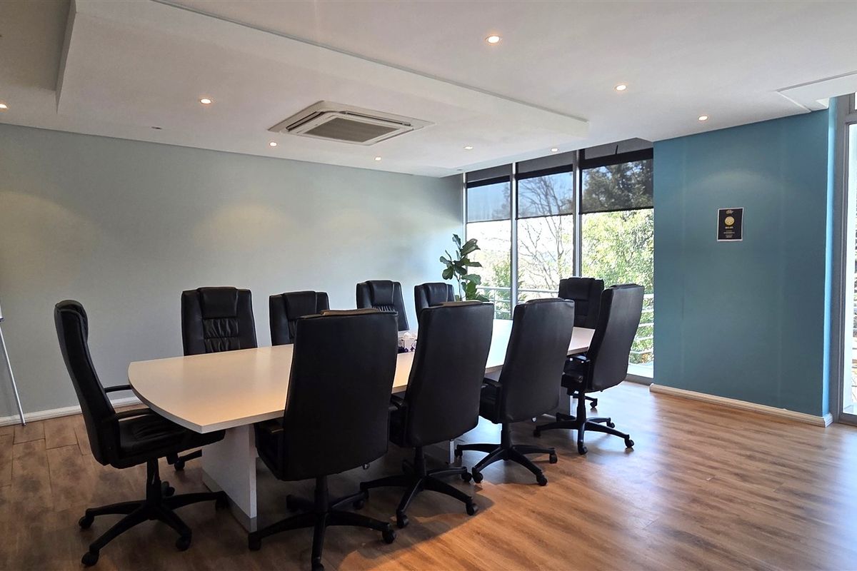 A professional office boardroom featuring laminate wood flooring, recessed ceiling lighting, integrated air conditioning, and large windows providing natural light and exterior views.