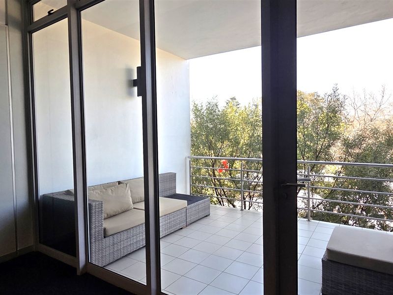 A covered balcony featuring tiled flooring, a stainless steel balustrade, and large sliding glass doors providing access to the office interior.
