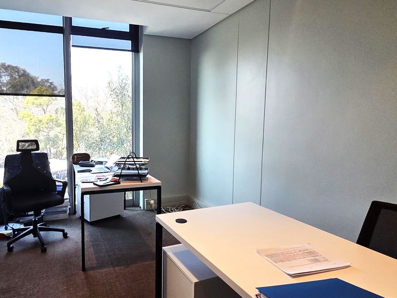 A bright, professional office space featuring floor-to-ceiling windows that provide ample natural light and views of the surrounding greenery.