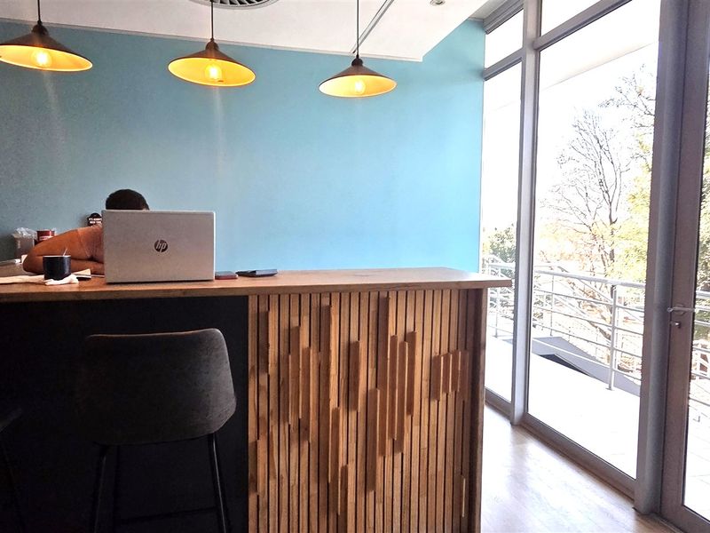Modern office space featuring a timber slat desk, pendant lighting, and large floor-to-ceiling windows providing ample natural light and exterior views.
