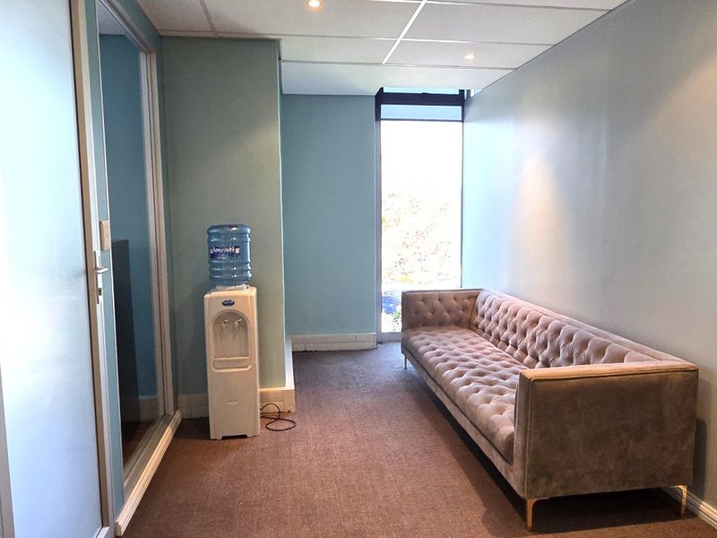 A functional office waiting area featuring carpeted flooring, a suspended ceiling with recessed lighting, and a glass partition wall.