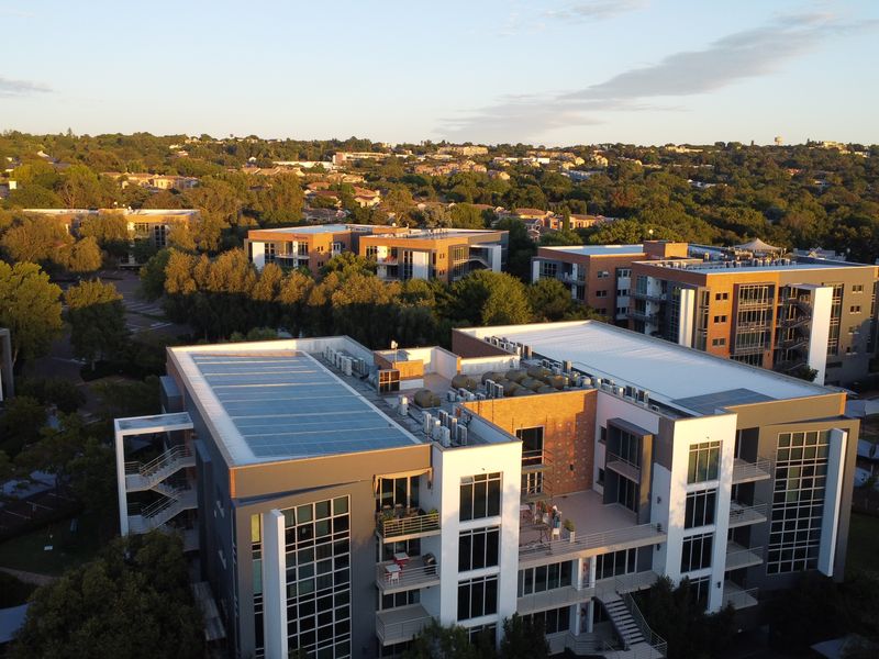Aerial view of a modern multi-story office complex featuring rooftop solar panels, HVAC systems, and extensive glass facade detailing.