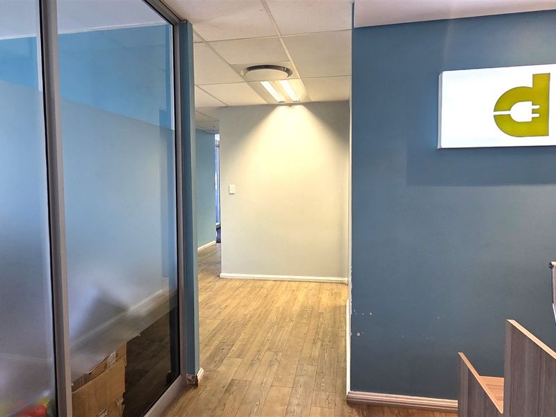 Professional office entrance featuring a glass partition, laminate flooring, and a branded wall-mounted sign in a well-lit, modern workspace.