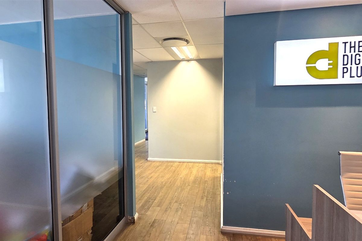 Professional office entrance featuring a glass partition, laminate flooring, and a branded wall-mounted sign in a well-lit, modern workspace.