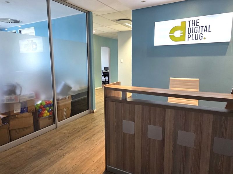 Professional office reception area featuring a built-in reception desk, modern glass partitioning, and clean laminate flooring with integrated lighting.