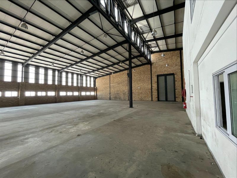 Spacious industrial warehouse featuring high ceilings with exposed steel trusses, brick wall accents, concrete flooring, and ample natural light from clerestory windows.