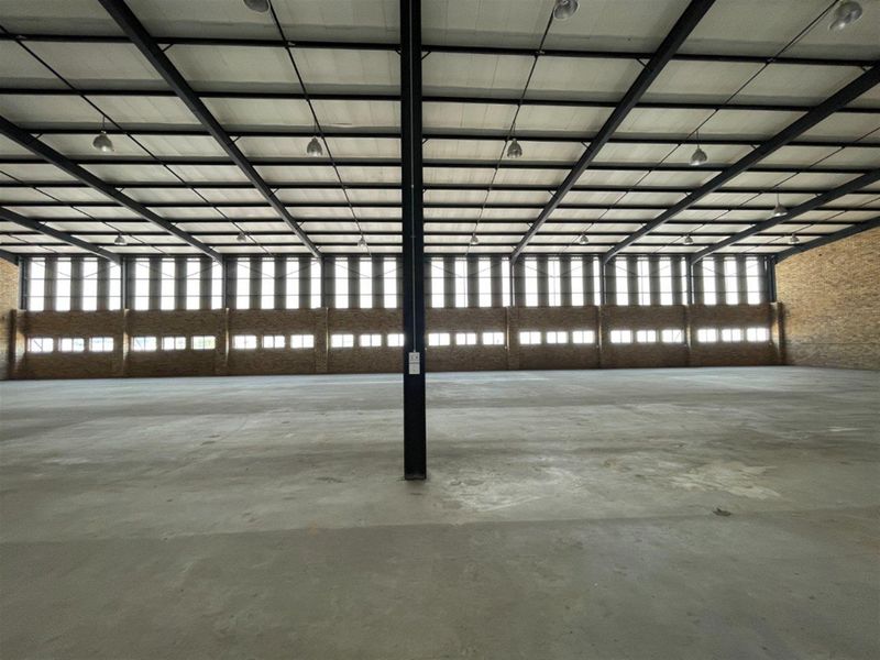 Spacious industrial warehouse featuring exposed steel framing, concrete flooring, and extensive natural light through clerestory windows.