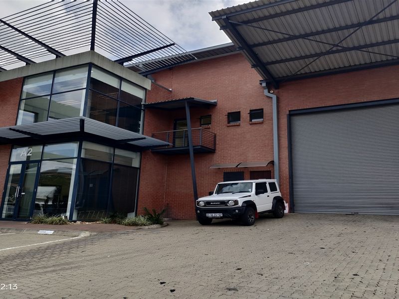 Modern industrial facility featuring a brick facade, large glass curtain wall, and a high-clearance roller shutter door with paved driveway access.