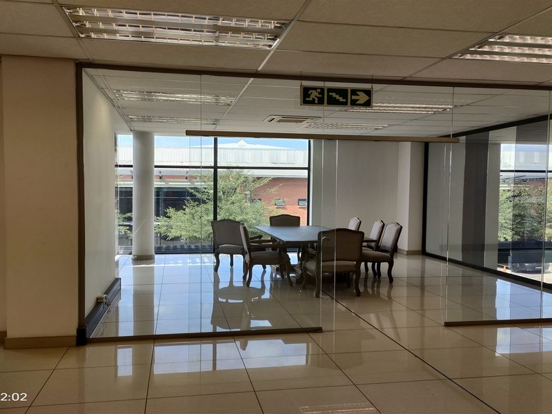 A modern office meeting room featuring glass partition walls, tiled flooring, and a suspended ceiling with recessed lighting, offering a professional workspace environment.