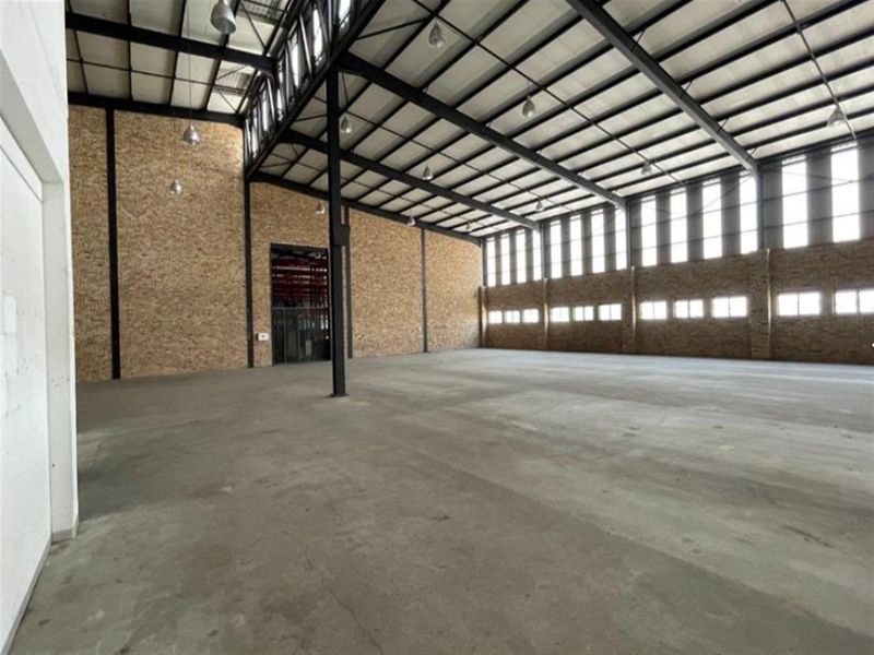 Spacious industrial warehouse unit featuring high ceilings with exposed steel trusses, brick wall finishes, concrete flooring, and ample natural light from clerestory windows.