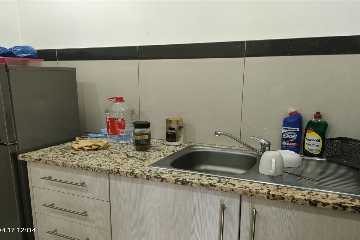 A functional kitchen area featuring a granite countertop, stainless steel sink with mixer tap, and tiled backsplash with built-in cabinetry.