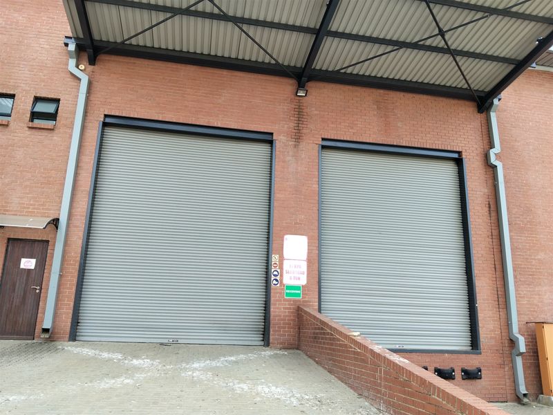 Industrial loading bay area featuring two large roller shutter doors, a covered canopy, and brick exterior wall construction.