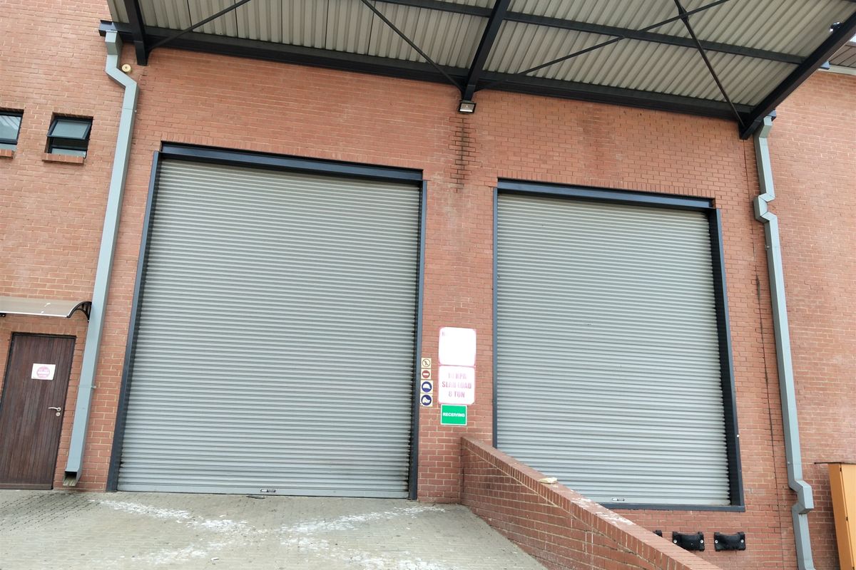 Industrial loading bay area featuring two large roller shutter doors, a covered canopy, and brick exterior wall construction.