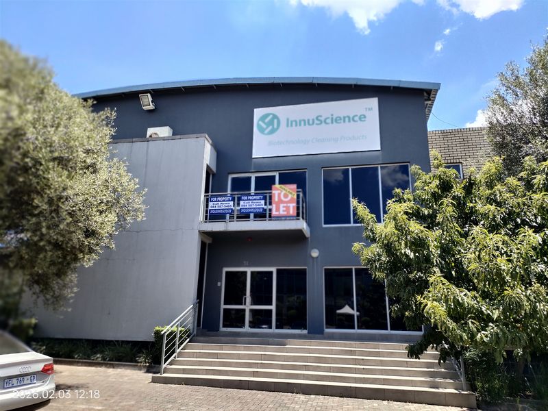 Front elevation of an industrial building featuring large glass windows, a metal staircase, and prominent signage, set within a paved exterior area.