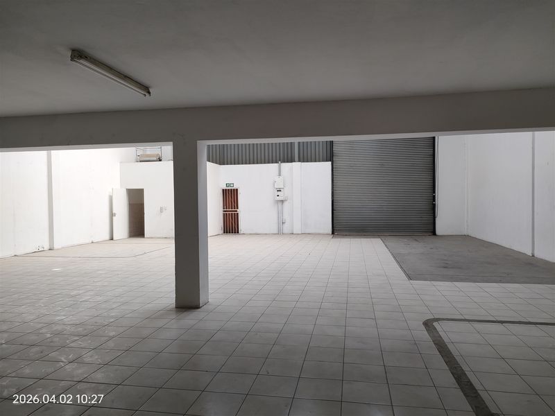 Spacious industrial utility area featuring tiled flooring, a large roller shutter door, and secure access points, suitable for storage or workshop operations.