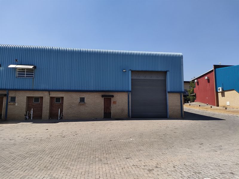 Industrial warehouse exterior featuring a large roller shutter door, face brick facade, and blue corrugated metal cladding with a paved driveway.